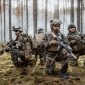 Four fully equipped, middle-aged soldiers in camouflage uniforms form a line, ready to fire, aiming with their rifles. A military operation in action, a unit standing in a dense forest.