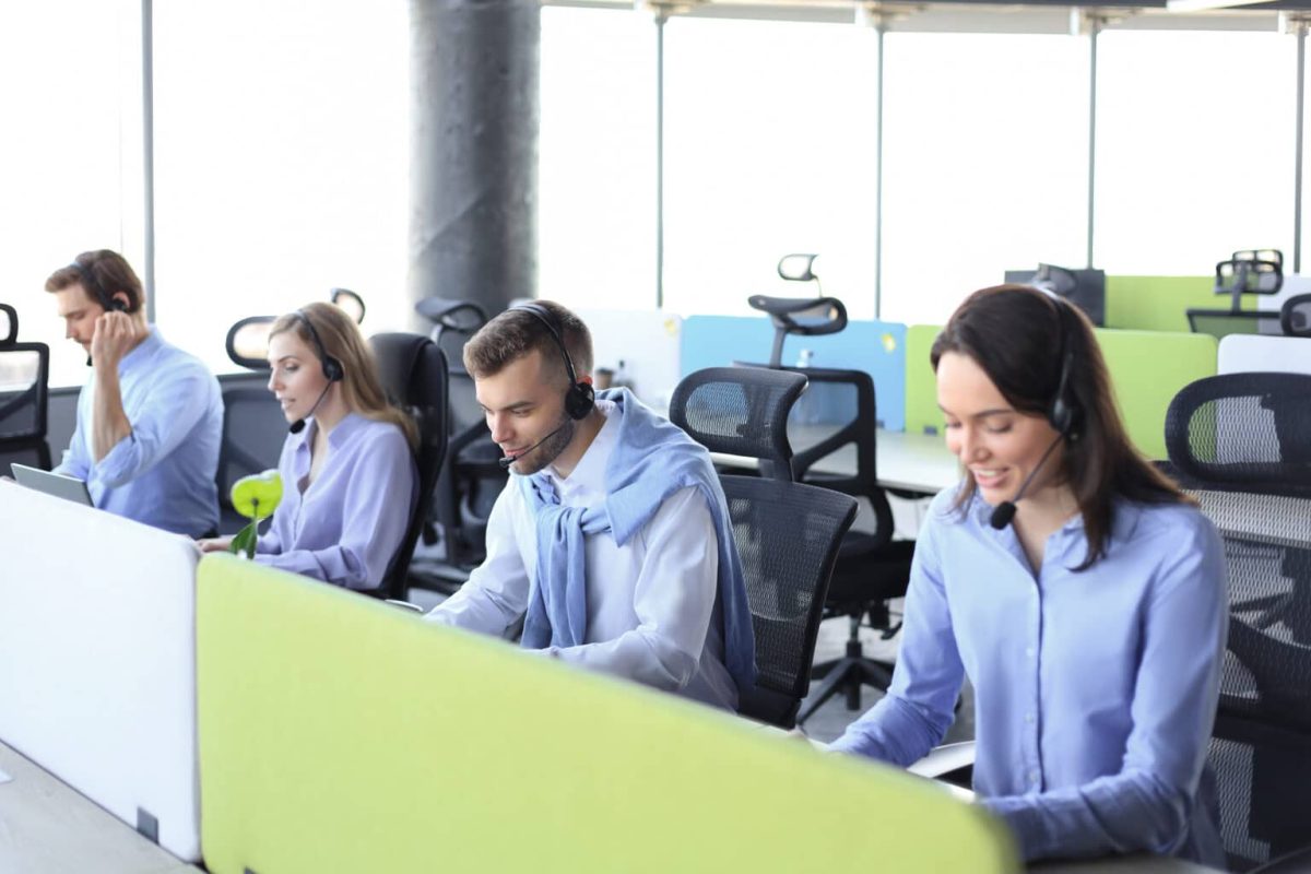Young employee working with a headset and accompanied by her team